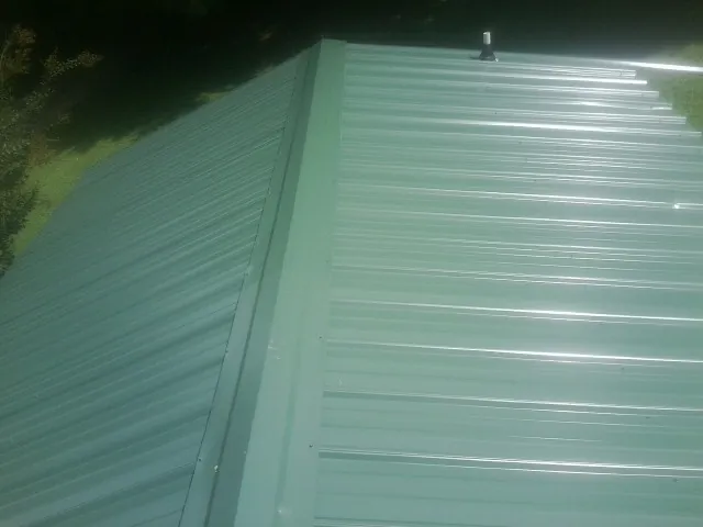 New green metal panels meeting at the ridge of a roof — Flat Roof Repair work by our crew in Oak City