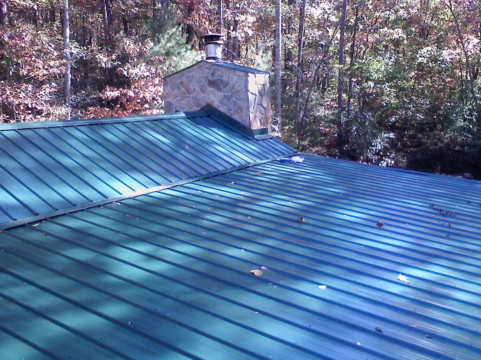 New green metal roof and stone chimney surrounded by autumn woods in Oak City