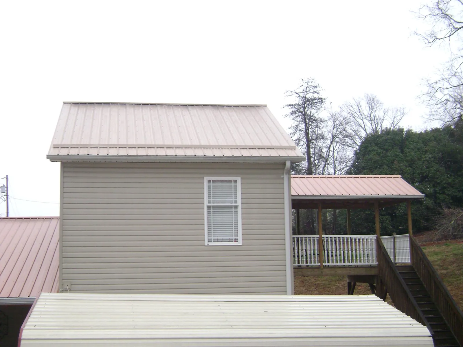 Tan metal roofs on a two story addition and attached porch, from a Roof Replacement job in Oak City
